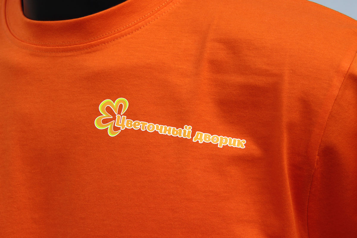 Увеличенная Фотография фрагмента оранжевой футболки с логотипом Цветочный дворик на груди